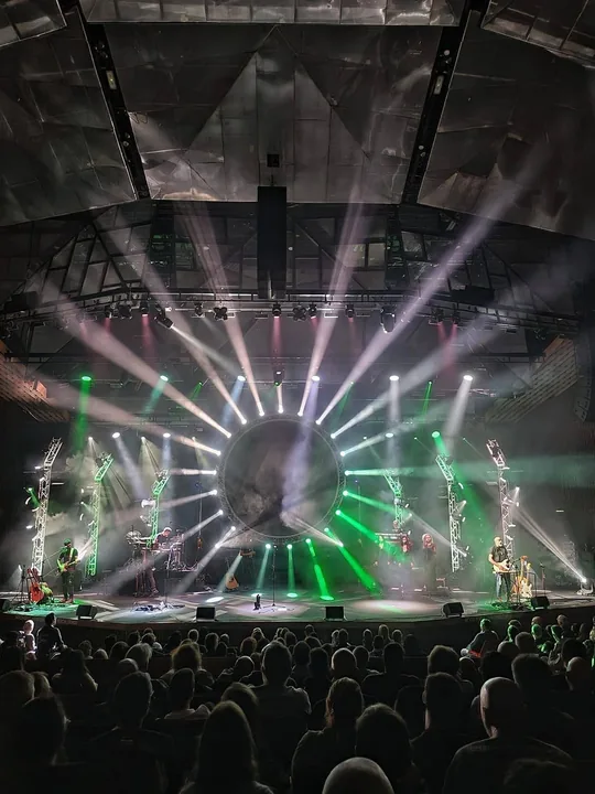 A full hall facing the stage under a ring of light beams